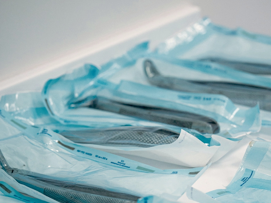 Instrumentos odontológicos em embalagens seladas de esterilização, empilhados sobre a bancada.