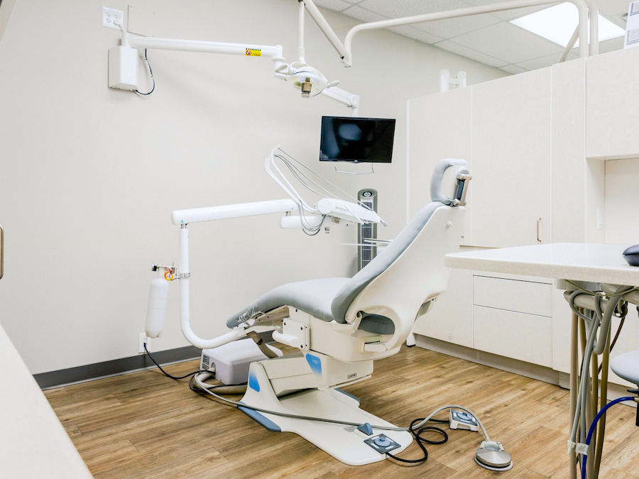 Sala de atendimento clara, com cadeira odontológica, foco cirúrgico, monitor na parede e piso de madeira.