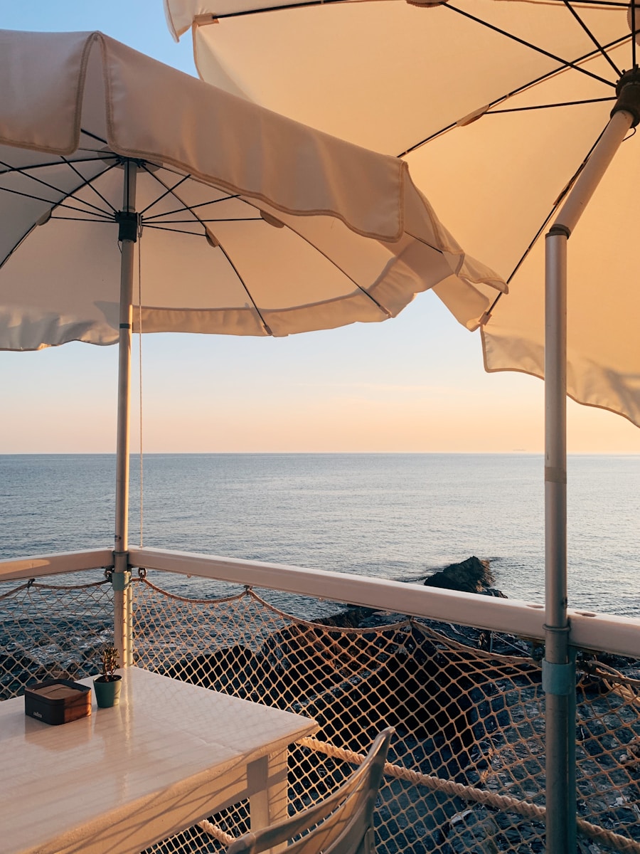 Mesa posta sob guarda-sol num deck à beira-mar, com o sol baixo sobre a água.